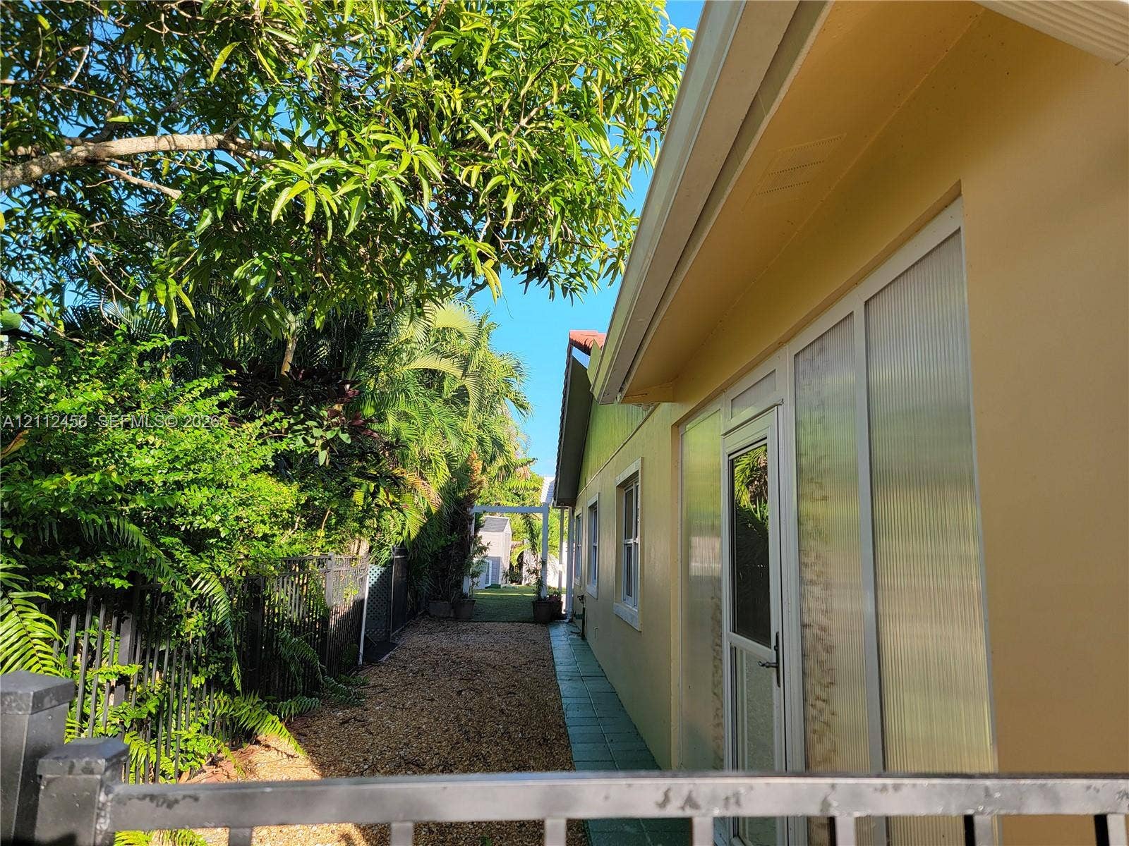 3961 NW 110th Avenue, #3961, Coral Springs, Coral Springs, FL 33065 Exterior side yard featuring a paved walkway, gravel ground cover, privacy fencing, and mature vegetation