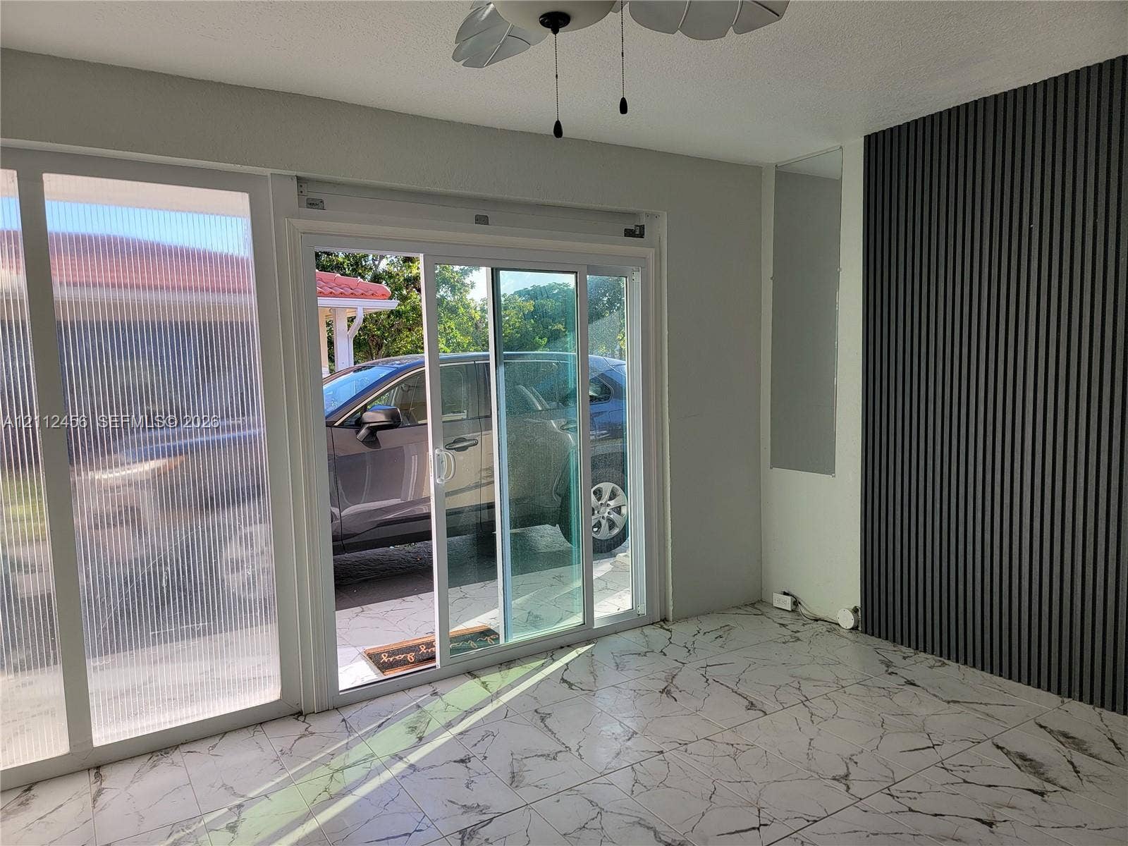 3961 NW 110th Avenue, #3961, Coral Springs, Coral Springs, FL 33065 Interior space featuring large-format marbled floor tile, a dark wood-slat accent wall, sliding glass doors, and a ceiling-mounted fan