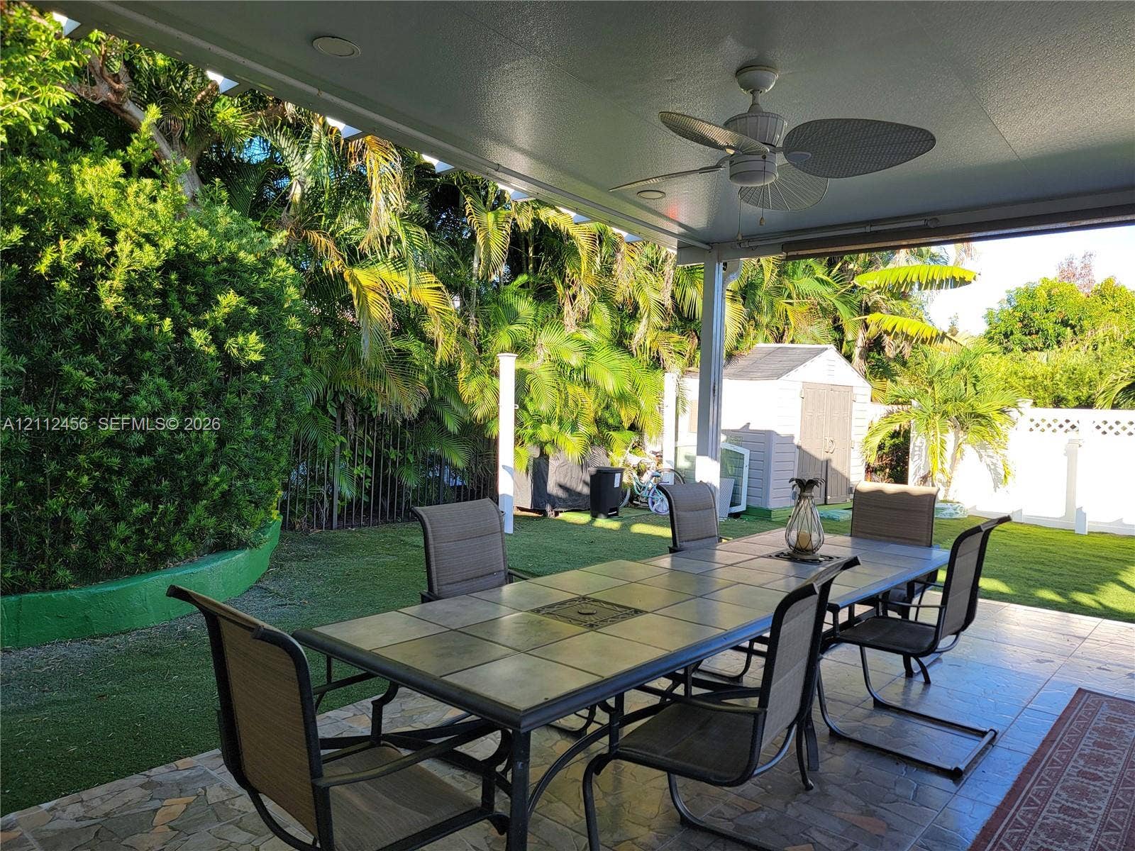 3961 NW 110th Avenue, #3961, Coral Springs, Coral Springs, FL 33065 Covered rear patio featuring a tile-paved floor and ceiling-mounted fan, overlooking a lawn with mature landscaping and a detached storage shed