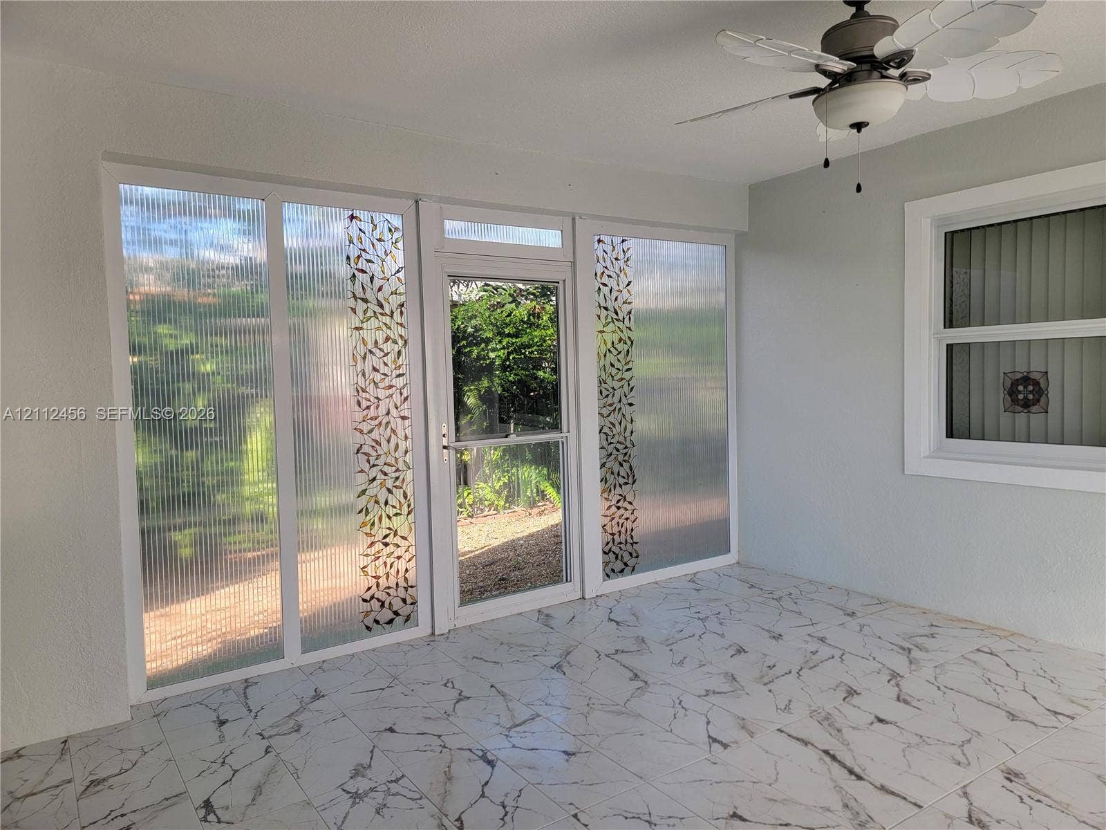 3961 NW 110th Avenue, #3961, Coral Springs, Coral Springs, FL 33065 Enclosed space featuring large format stone-patterned tile flooring, textured glass panels with decorative leaf detailing, a central full-view storm door, and a ceiling-mounted fan with integrated light fixture