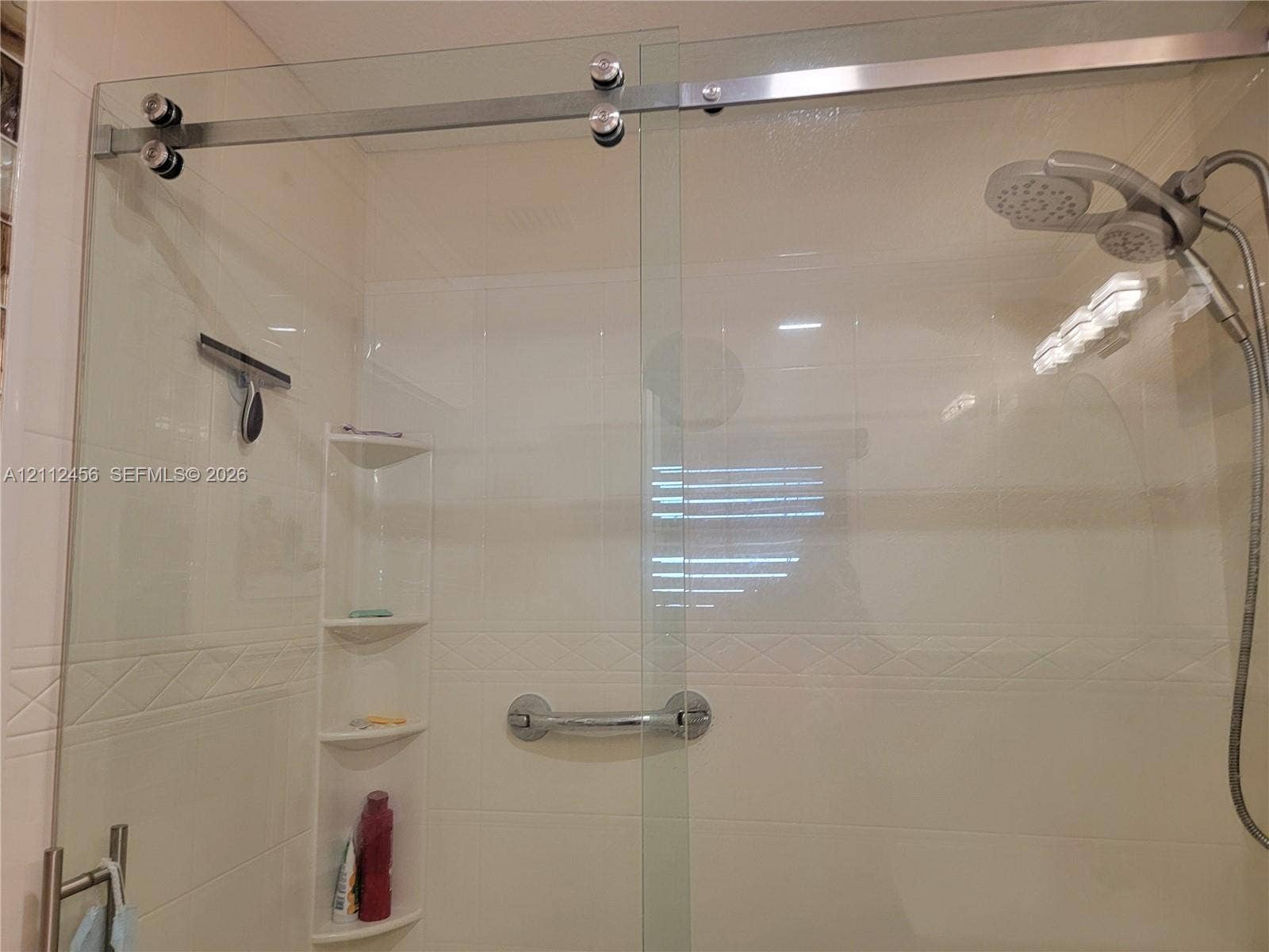 3961 NW 110th Avenue, #3961, Coral Springs, Coral Springs, FL 33065 Frameless glass shower enclosure featuring a stainless steel sliding door system, integrated corner shelving, chrome grab bar, and adjustable handheld shower head