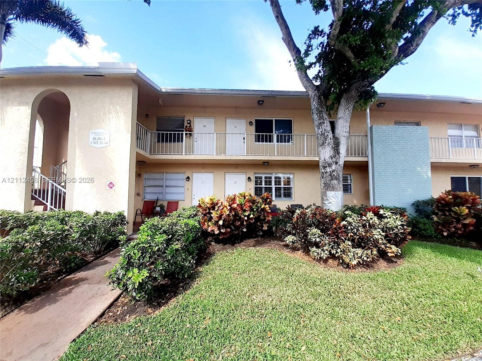 2607 NE 8th Avenue, #32, Wilton Manors, FL 33334 Two-story stucco exterior featuring a second-level balcony with metal railing, manicured landscaping, and a concrete walkway