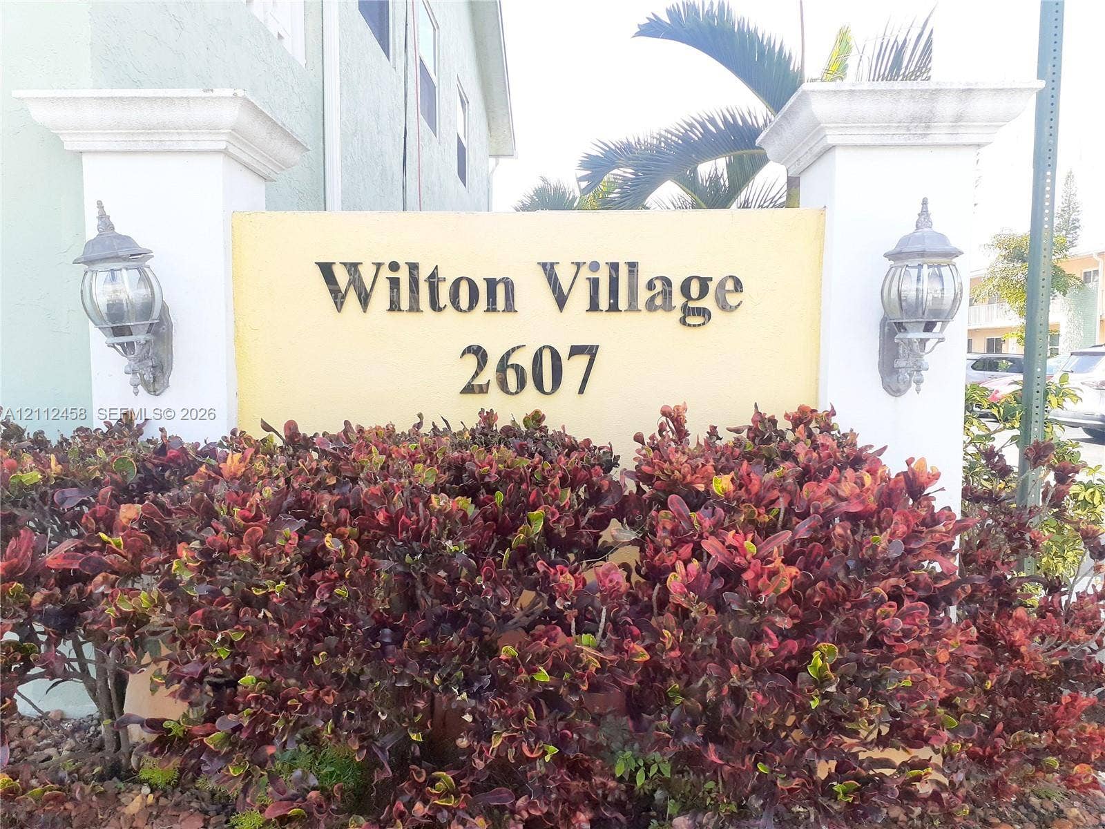 2607 NE 8th Avenue, #32, Wilton Manors, FL 33334 Entrance monument featuring stucco pillars, wall-mounted coach-style lighting, and mature landscape shrubbery