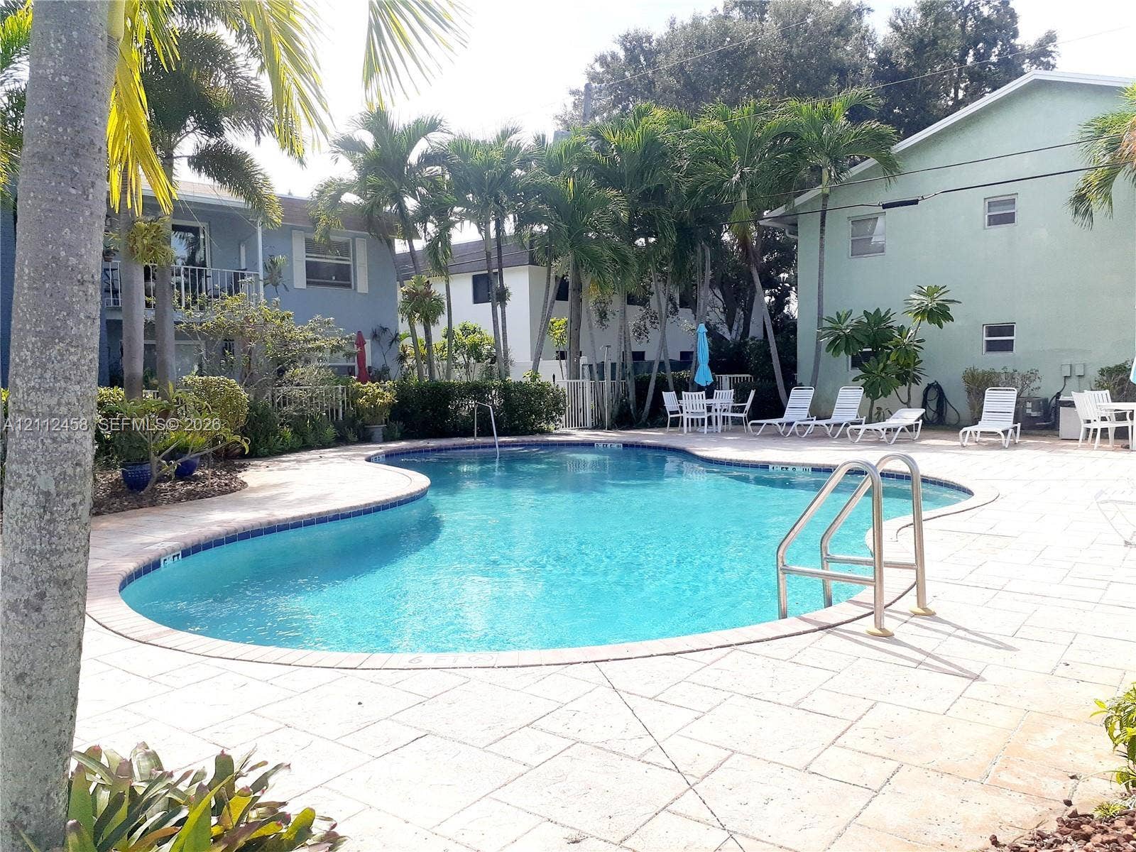 2607 NE 8th Avenue, #32, Wilton Manors, FL 33334 Curved swimming pool with a stone paver deck, metal ladder, and mature palm tree landscaping