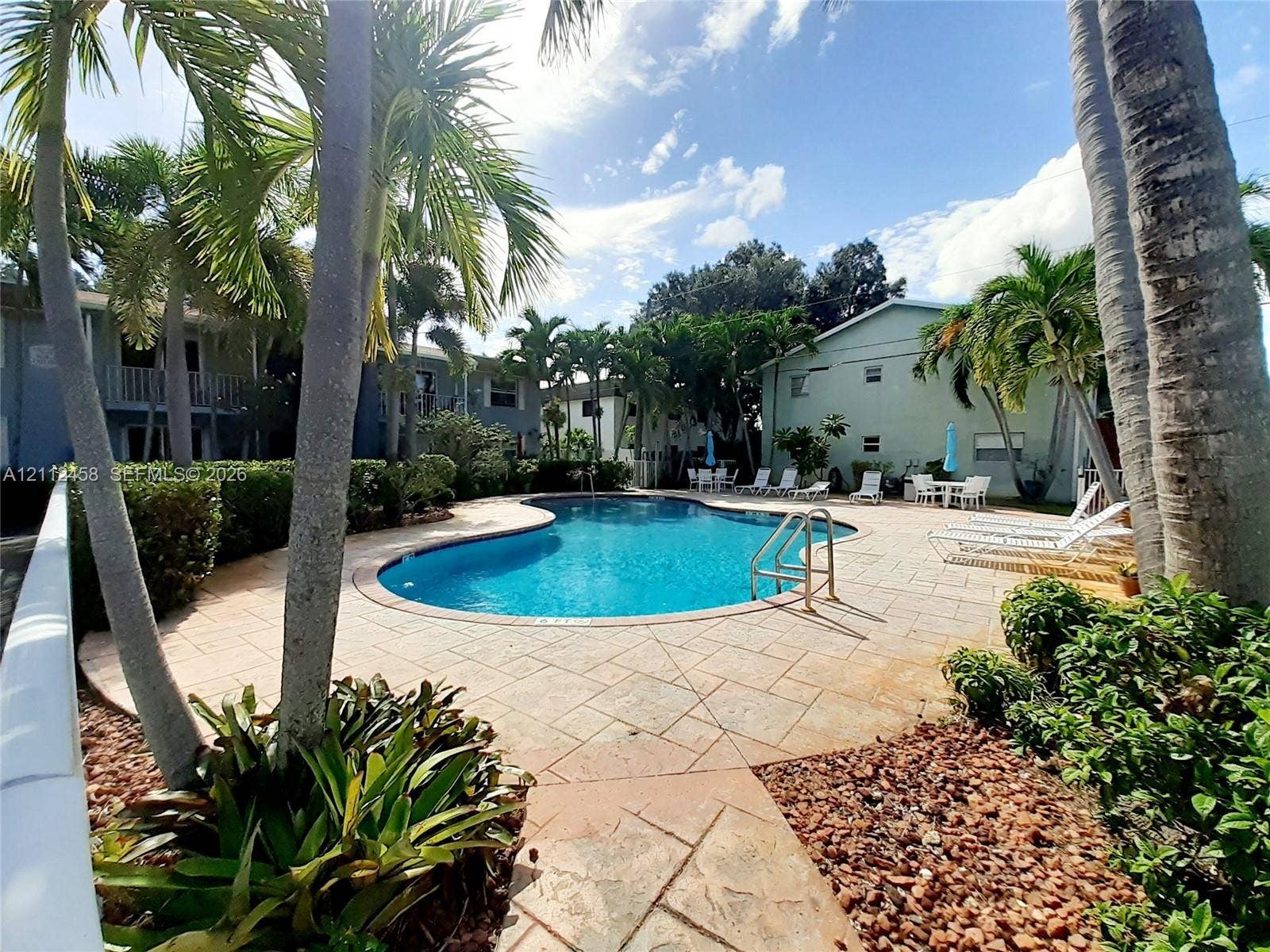 2607 NE 8th Avenue, #32, Wilton Manors, FL 33334 Swimming pool featuring a stone-paver deck, metal pool ladder, mature palm trees, and landscaped shrubbery