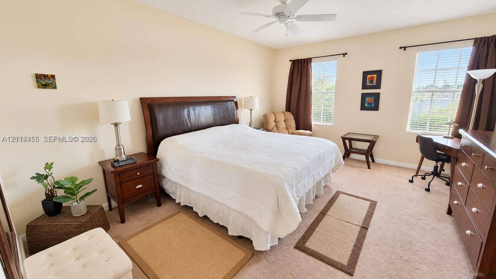 Neutral-toned bedroom featuring carpeting, two double-hung windows, and a ceiling-mounted fan