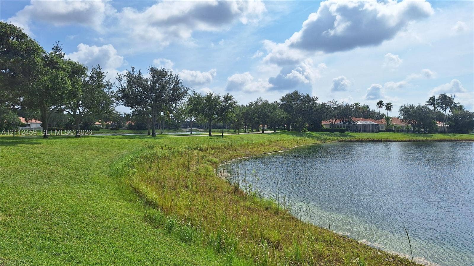 Waterfront property featuring a manicured lawn, mature trees, and natural shoreline