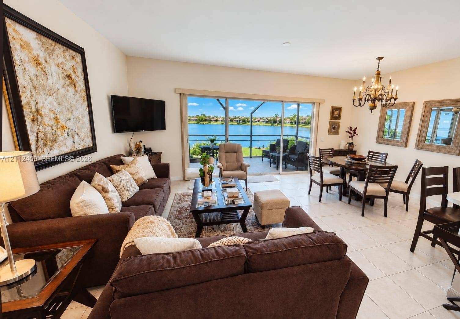 Open-concept living and dining area featuring large-format tile flooring, a multi-arm chandelier, and sliding glass doors revealing water scenery