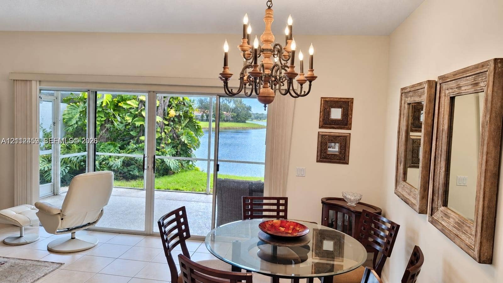 Multi-panel sliding glass doors, decorative multi-arm chandelier, and ceramic tile flooring, with exterior access to a screened lanai and water backdrop