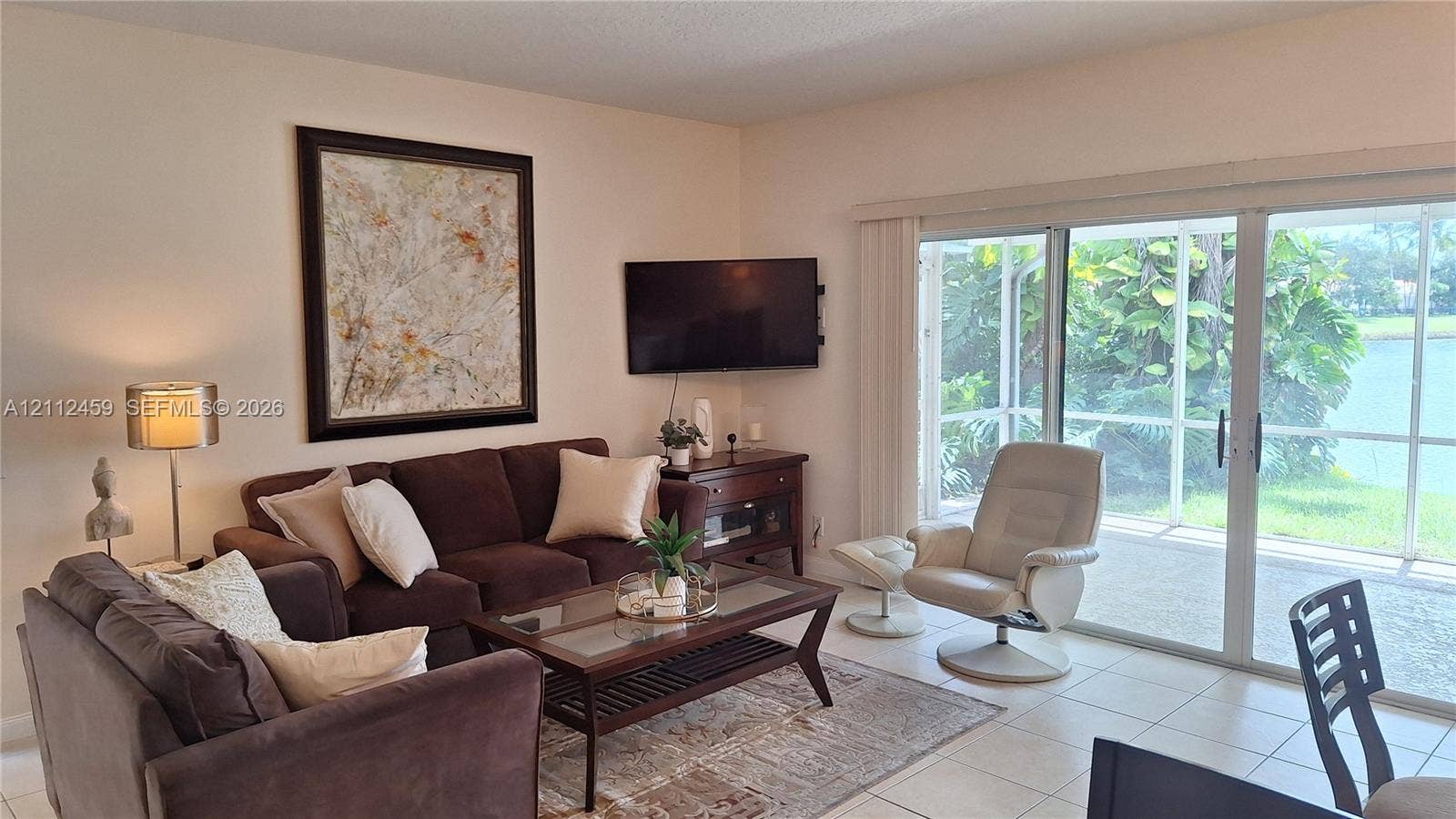 Living area featuring large-format ceramic tile flooring and floor-to-ceiling sliding glass doors opening to a screened lanai with water scenery
