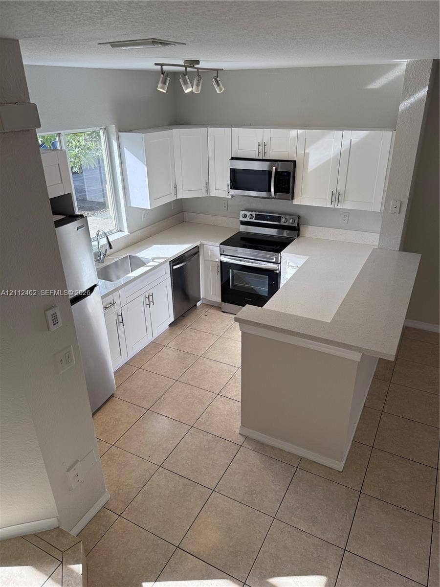 20439 NW 15th Avenue, #9, Miami Gardens, Miami Gardens, FL 33169 Kitchen featuring white shaker-style cabinetry, solid-surface countertops, tile flooring, stainless steel appliances, and track lighting