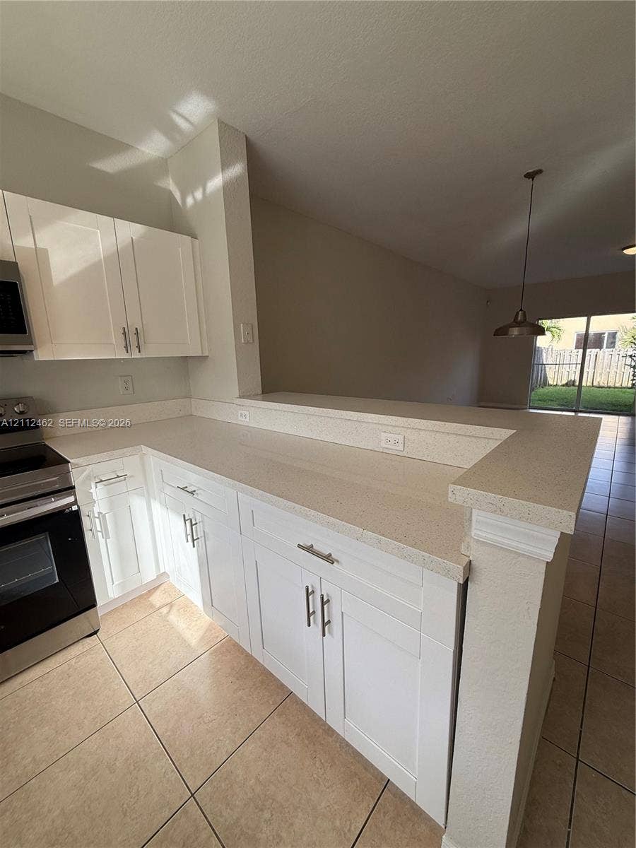 20439 NW 15th Avenue, #9, Miami Gardens, Miami Gardens, FL 33169 Kitchen featuring white shaker-style cabinetry, neutral stone-composite countertops, stainless steel appliances, ceramic tile flooring, and a breakfast bar