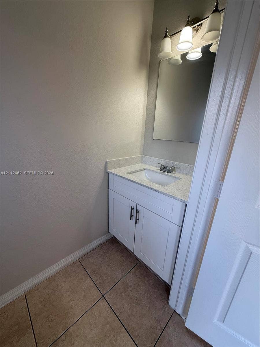 20439 NW 15th Avenue, #9, Miami Gardens, Miami Gardens, FL 33169 Bathroom vanity featuring white shaker-style cabinetry, solid-surface countertop with an integrated basin, three-light fixture, and ceramic tile flooring