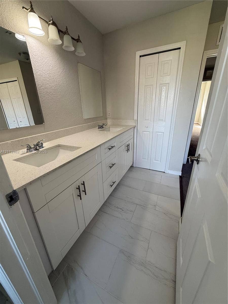 20439 NW 15th Avenue, #9, Miami Gardens, Miami Gardens, FL 33169 Dual vanity featuring a light-toned stone-composite countertop, white shaker-style cabinetry with matte black hardware, integrated rectangular basins, and large format rectified tile flooring