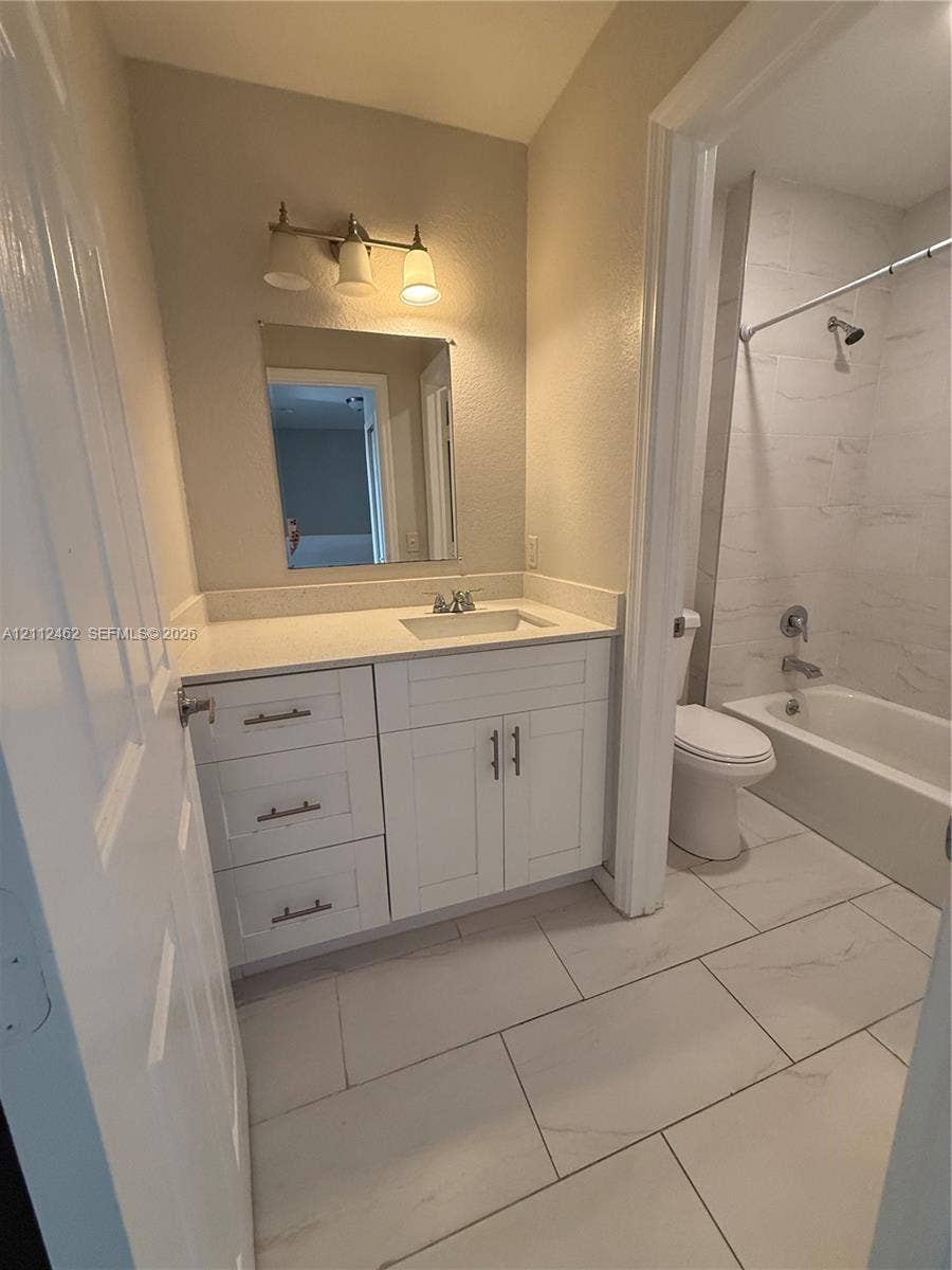 20439 NW 15th Avenue, #9, Miami Gardens, Miami Gardens, FL 33169 White vanity with stone-look countertop, integrated rectangular sink, three-light wall-mounted fixture, and large-format tile flooring