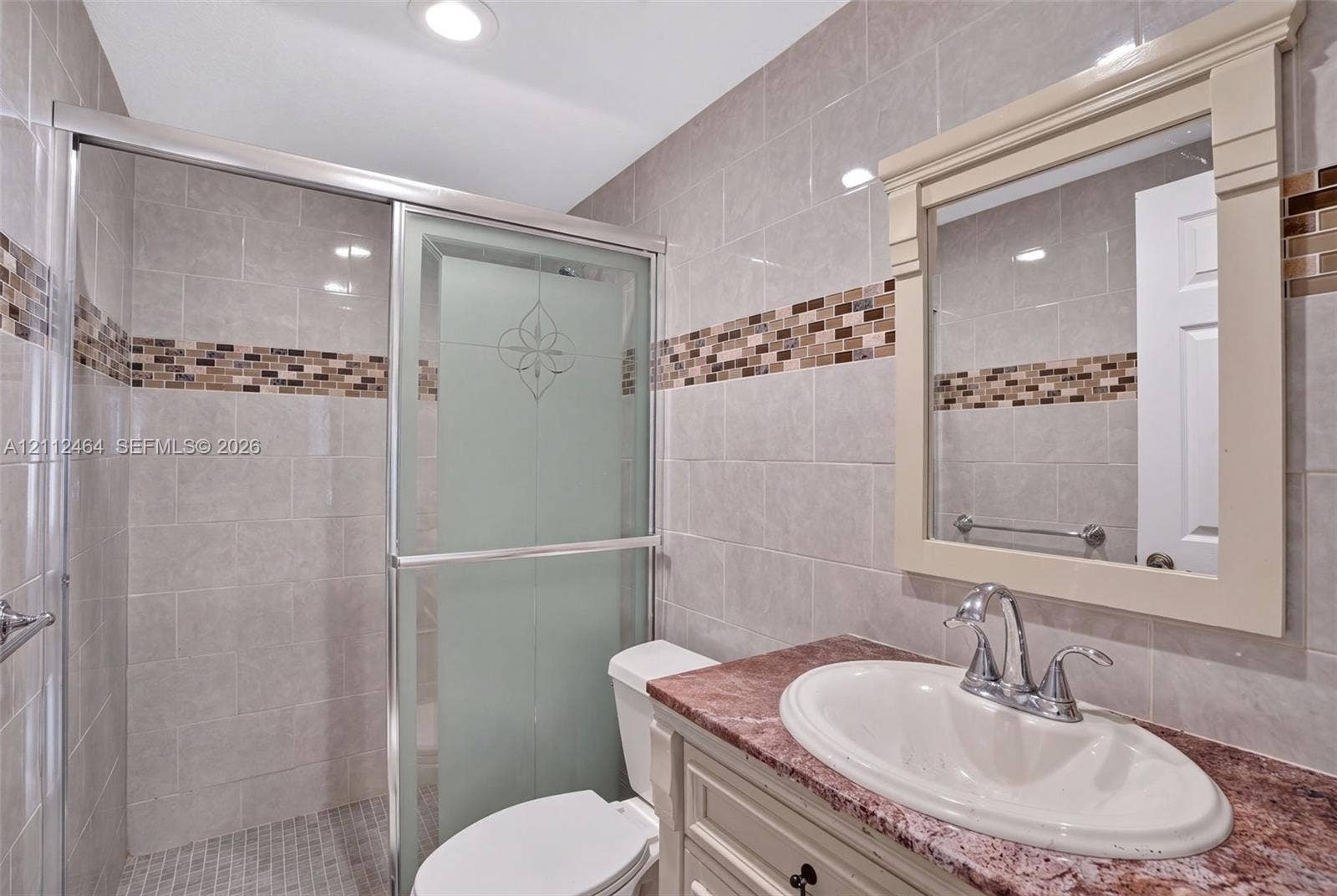 Bathroom featuring a vanity with a stone countertop, an integrated sink, a framed wall mirror, a shower with a sliding glass door, and decorative tile accents
