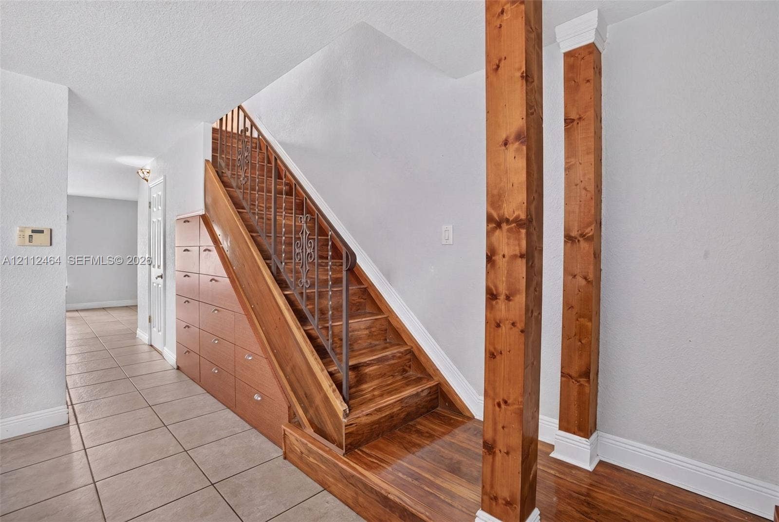 Staircase featuring wood treads, ornate metal handrail, and integrated under-stair cabinetry, accented by two prominent wood-finish structural columns