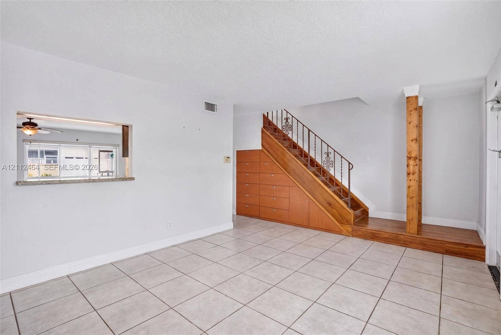 Interior space featuring large-format tile flooring, built-in under-stair cabinetry with wood finish, decorative metal stair railing, and a pass-through window with a stone-finish ledge