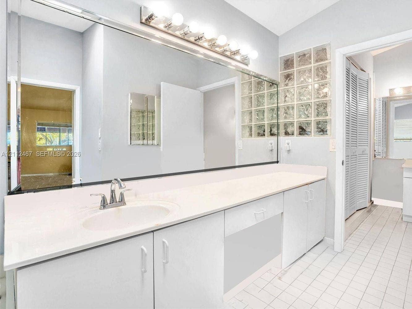 250 NE 212th Street, Miami, Miami, FL 33179 Extended vanity featuring a smooth surface countertop, integrated oval sink, full-width wall mirror, chrome-finish faucet, and privacy glass block window