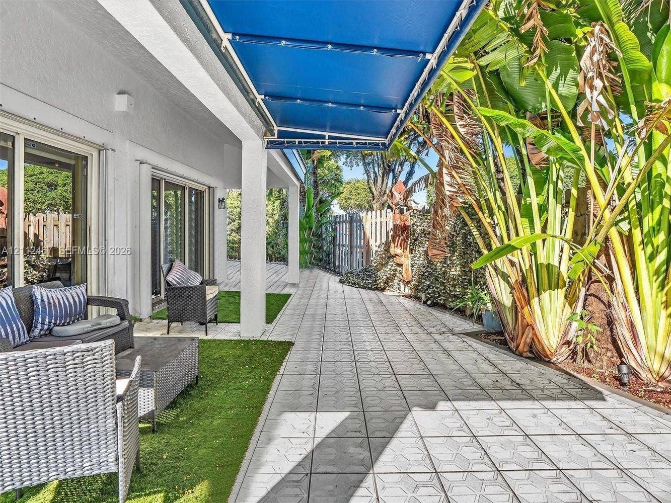 250 NE 212th Street, Miami, Miami, FL 33179 Covered outdoor patio featuring retractable blue fabric awning, patterned tile flooring, and integrated artificial turf sections