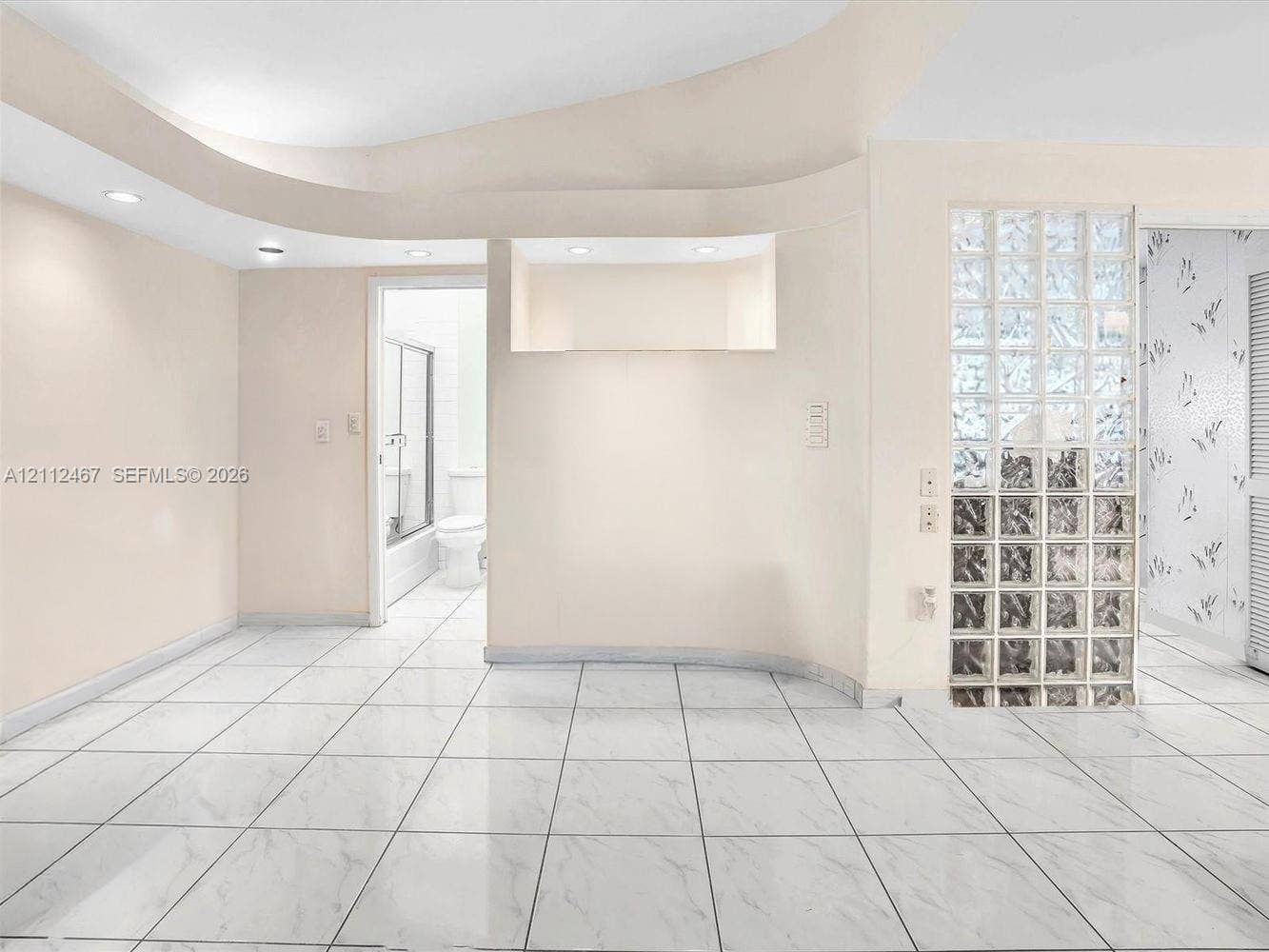 250 NE 212th Street, Miami, Miami, FL 33179 Interior space featuring large-format tile flooring, a curved architectural ceiling detail with recessed lighting, a built-in recessed wall niche, and a decorative glass block partition wall
