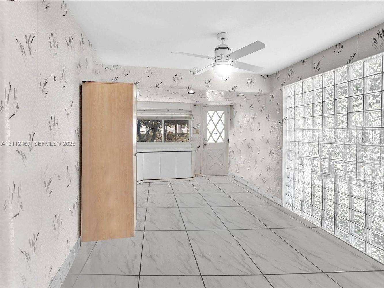 250 NE 212th Street, Miami, Miami, FL 33179 Room featuring large-format stone-patterned tile flooring, a floor-to-ceiling glass block wall, built-in light wood cabinetry, a white cross-panel door, and a ceiling-mounted light fixture with fan blades