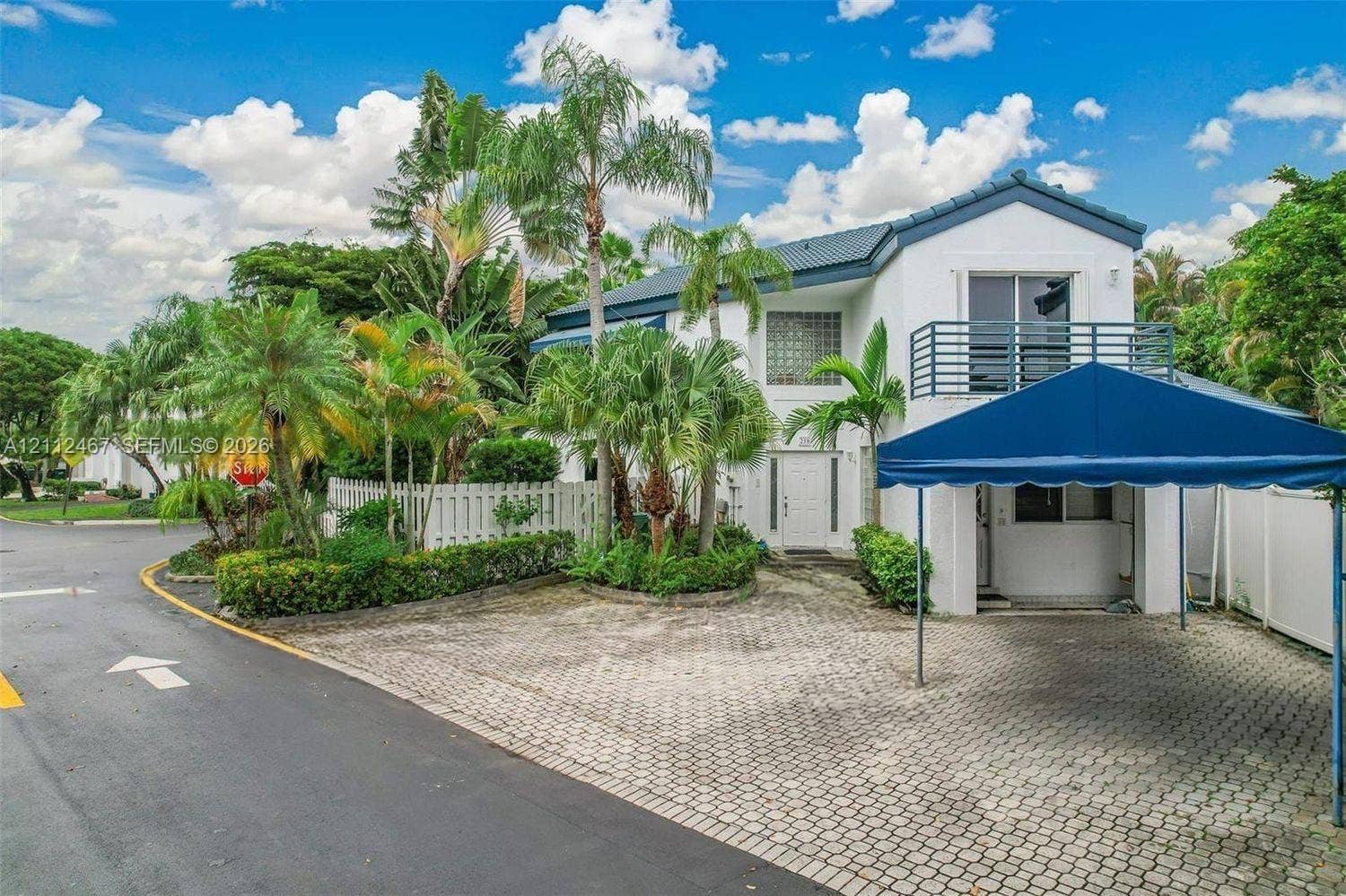 250 NE 212th Street, Miami, Miami, FL 33179 Two-story exterior featuring a paver driveway, covered carport, private balcony with metal railing, and mature palm landscaping