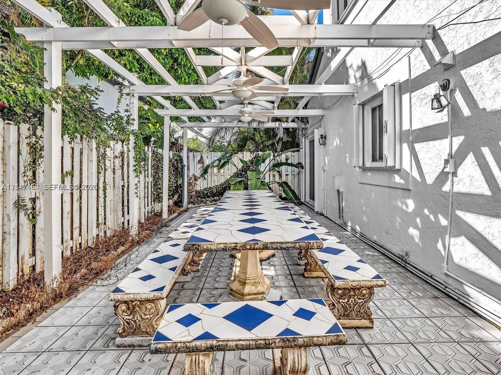 250 NE 212th Street, Miami, Miami, FL 33179 Outdoor patio featuring a white pergola with ceiling-mounted fans, geometric tile flooring, built-in tile-topped dining surfaces, and perimeter wood fencing