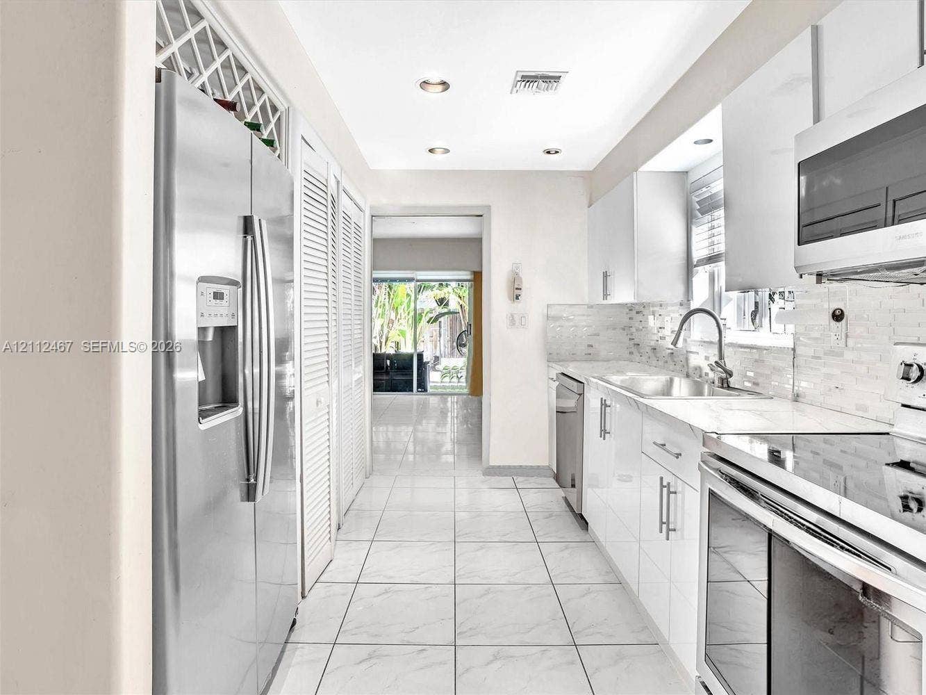 250 NE 212th Street, Miami, Miami, FL 33179 Galley kitchen featuring high-gloss cabinetry, stainless steel appliances, a mosaic tile backsplash, and tile flooring