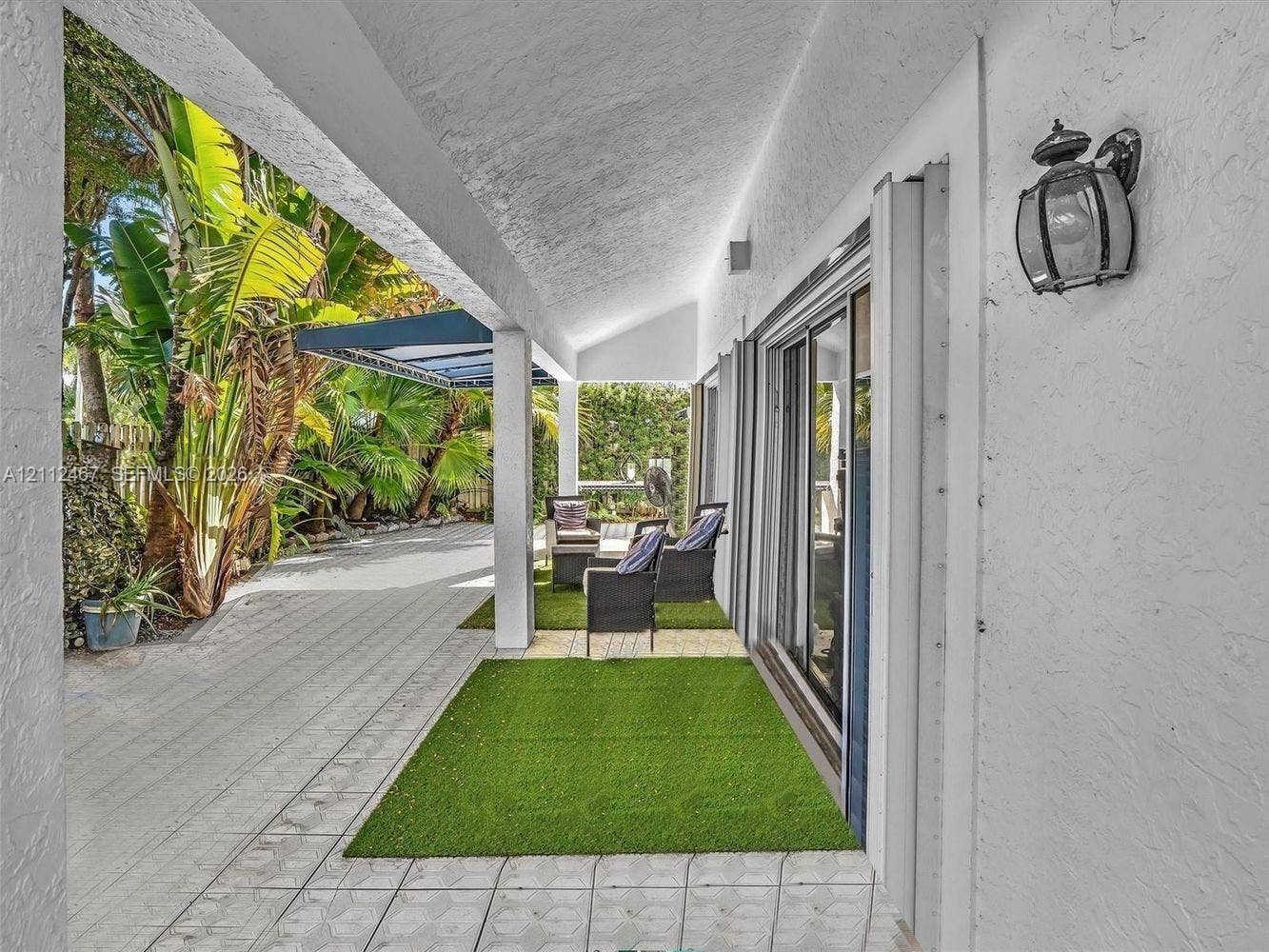 250 NE 212th Street, Miami, Miami, FL 33179 Covered patio featuring textured stucco exterior walls, light-toned paved flooring, an attached wall-mounted lantern light fixture, and floor-to-ceiling glass sliding doors
