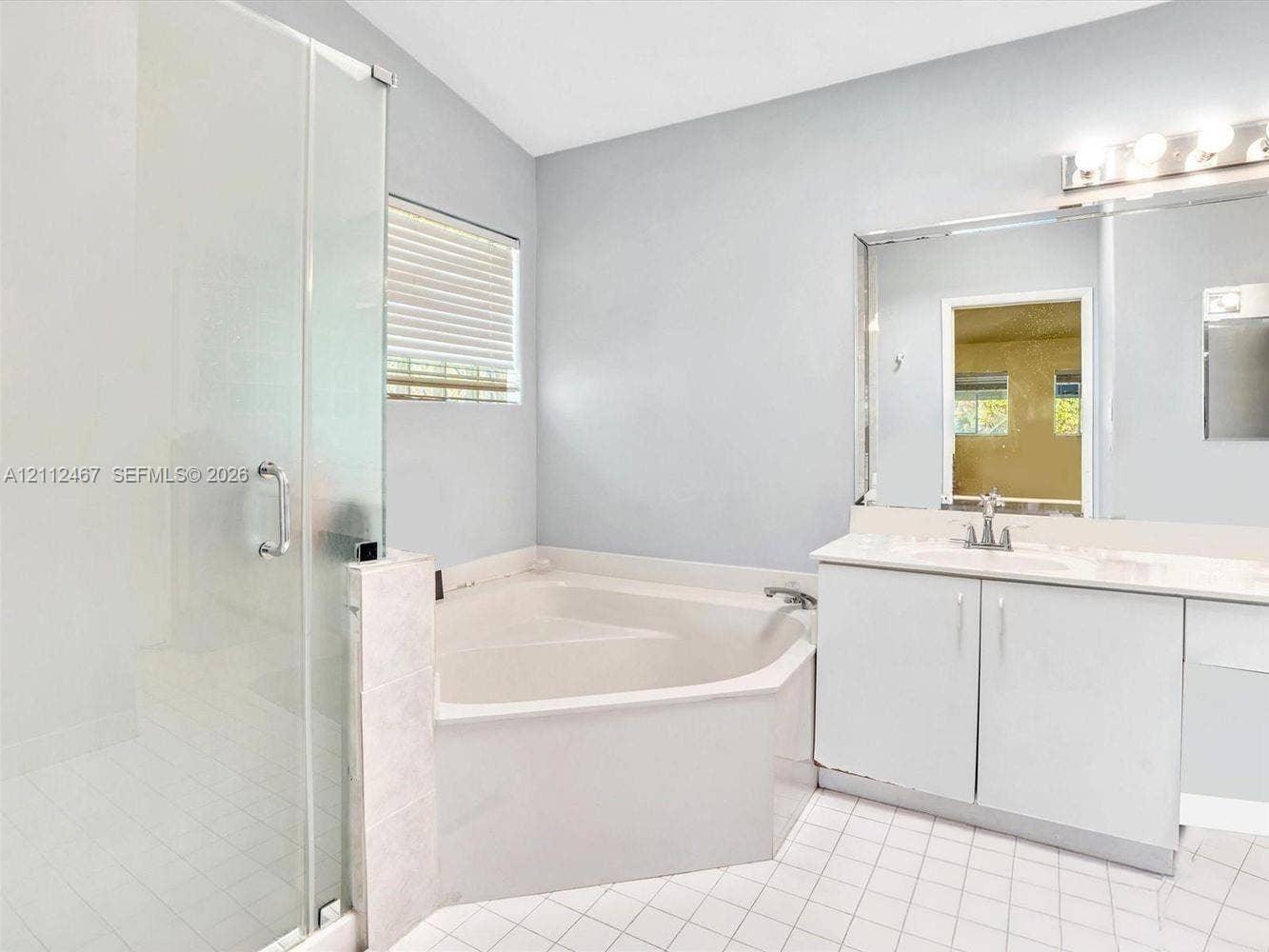 250 NE 212th Street, Miami, Miami, FL 33179 Glass-enclosed shower with tiled flooring, corner soaking tub, vanity with stone countertop, oversized wall-mounted mirror, and multi-bulb vanity lighting