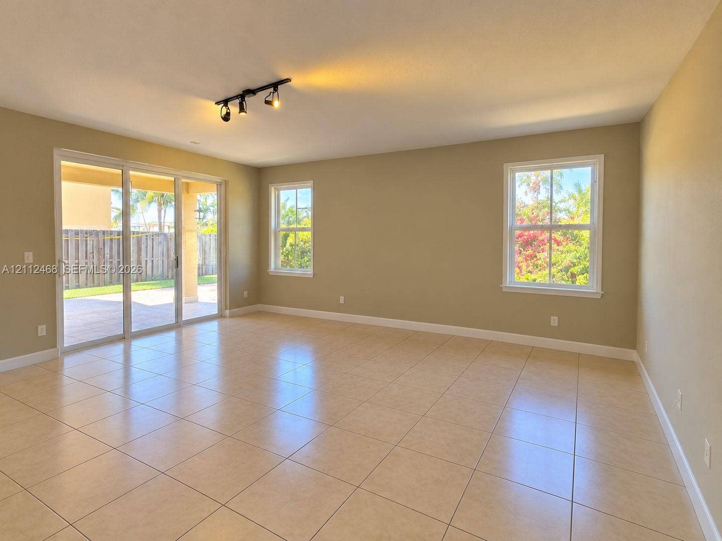 11009 NW 80th Lane, Doral, FL 33178 Open-concept interior featuring neutral tile flooring, multi-panel sliding glass doors, multi-pane windows, and a three-light track lighting fixture