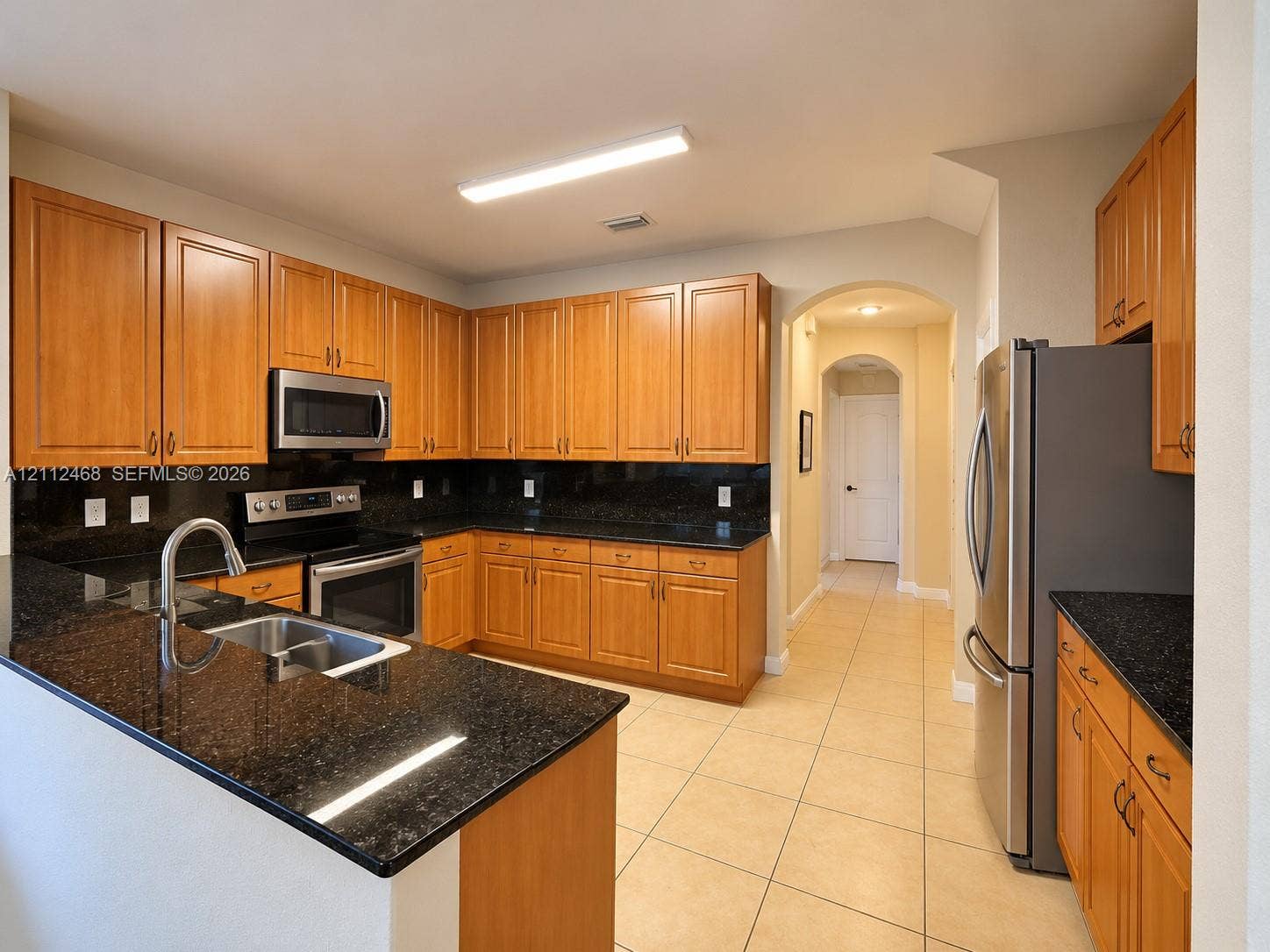 11009 NW 80th Lane, Doral, FL 33178 Kitchen featuring wood cabinetry, dark stone countertops, stainless steel appliances, tile flooring, and an arched doorway