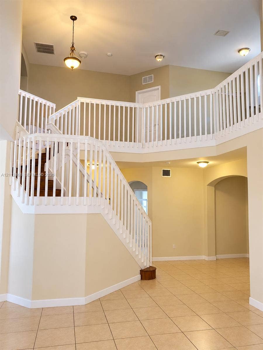 11009 NW 80th Lane, Doral, FL 33178 Two-story foyer featuring a vaulted ceiling, prominent staircase with a white balustrade, tile flooring, arched doorways, and a traditional pendant light fixture