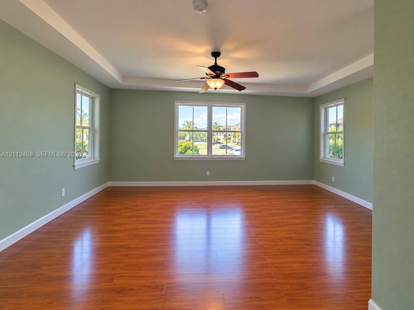 11009 NW 80th Lane, Doral, FL 33178 Room featuring wood-finish flooring, a tray ceiling, and a ceiling fan with integrated light fixture, illuminated by three double-hung windows