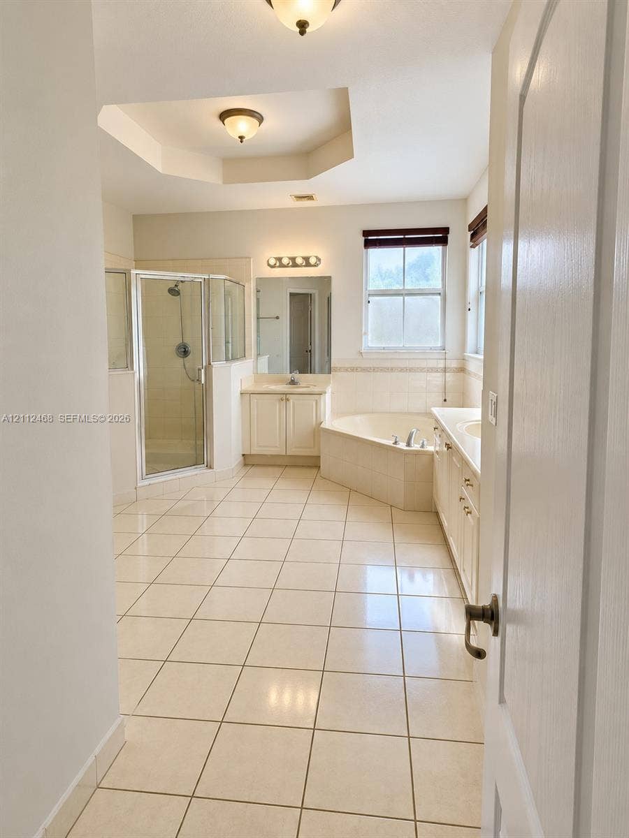 11009 NW 80th Lane, Doral, FL 33178 Ceramic tile flooring, corner soaking tub with tile surround, glass-enclosed shower, dual-sink vanity with light-colored cabinetry, and recessed tray ceiling