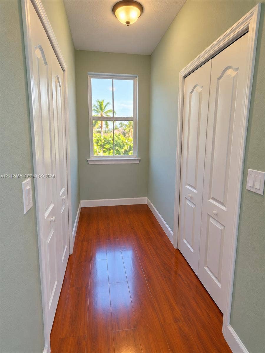 11009 NW 80th Lane, Doral, FL 33178 Wood-finish flooring, dual bifold closets with arched panel doors, and a double-hung window with exterior greenery