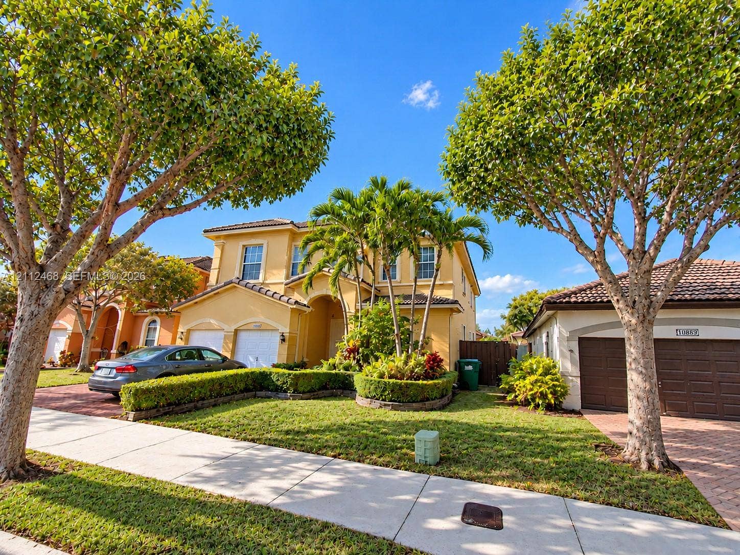 11009 NW 80th Lane, Doral, FL 33178 Two-story stucco exterior featuring a multi-gabled tile roof, arched entryway, and integrated two-car garage with brick-paver driveway