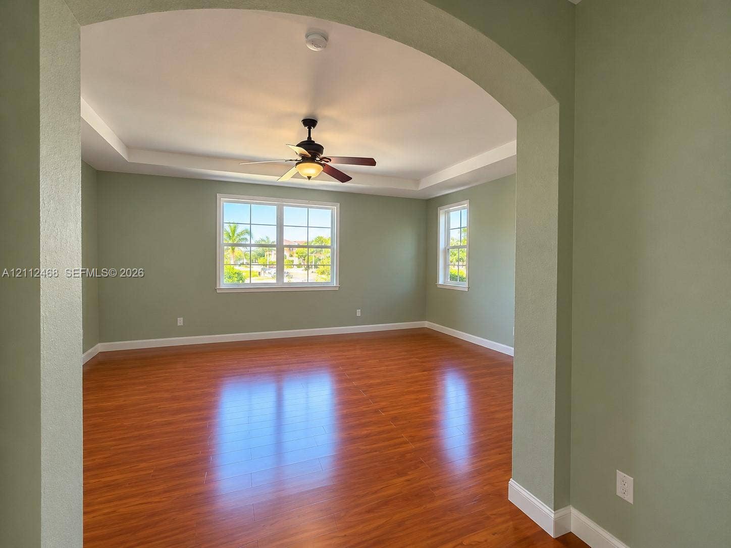 11009 NW 80th Lane, Doral, FL 33178 Interior space featuring wood-finish flooring, a tray ceiling with a center-mounted ceiling fan, and multi-lite windows framed by arched doorways