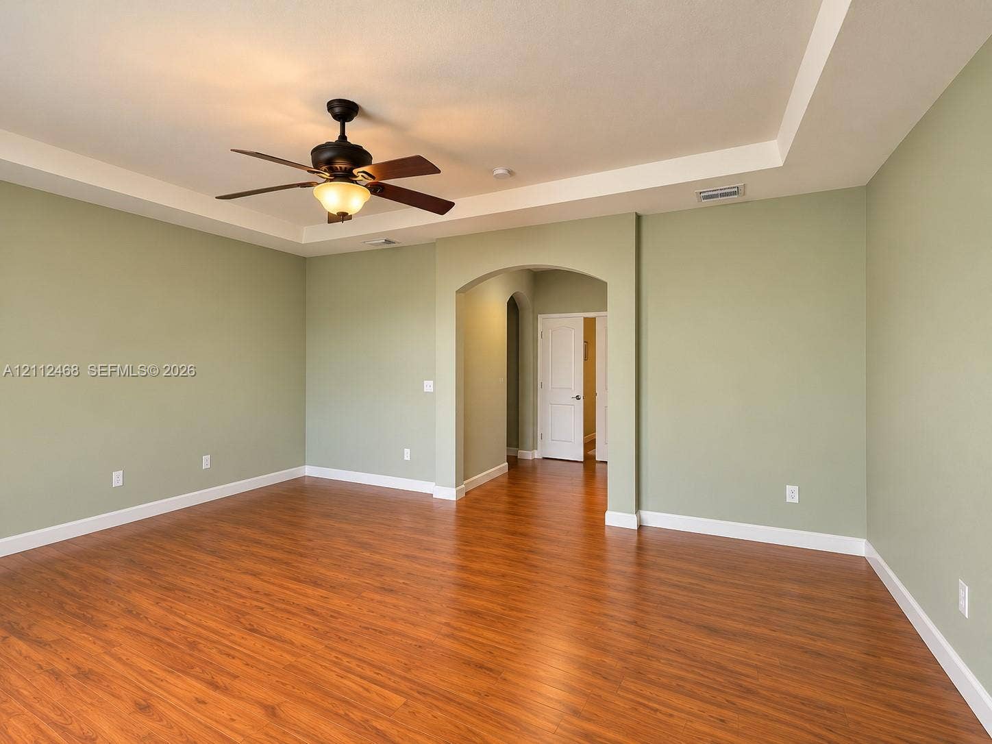 11009 NW 80th Lane, Doral, FL 33178 Room featuring wood-finish flooring, a tray ceiling, an arched entryway, and an attached ceiling fan with a light fixture