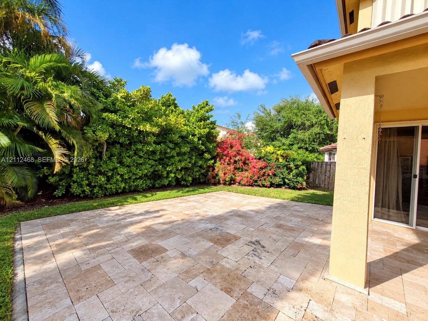 11009 NW 80th Lane, Doral, FL 33178 Covered patio featuring stone-tiled flooring, landscaped lawn, mature privacy hedges, and flowering shrubs