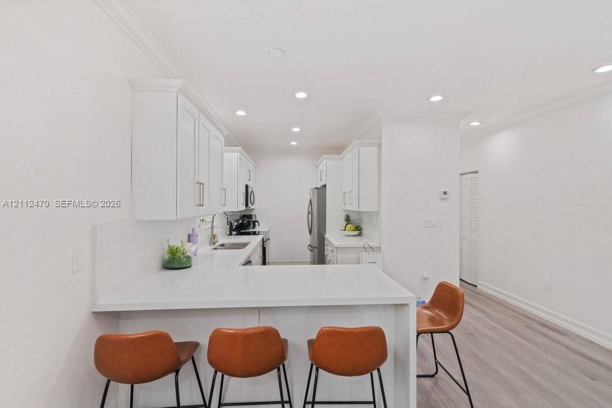 Kitchen featuring white cabinetry, solid-surface countertops, recessed ceiling lighting, and wood-finish flooring