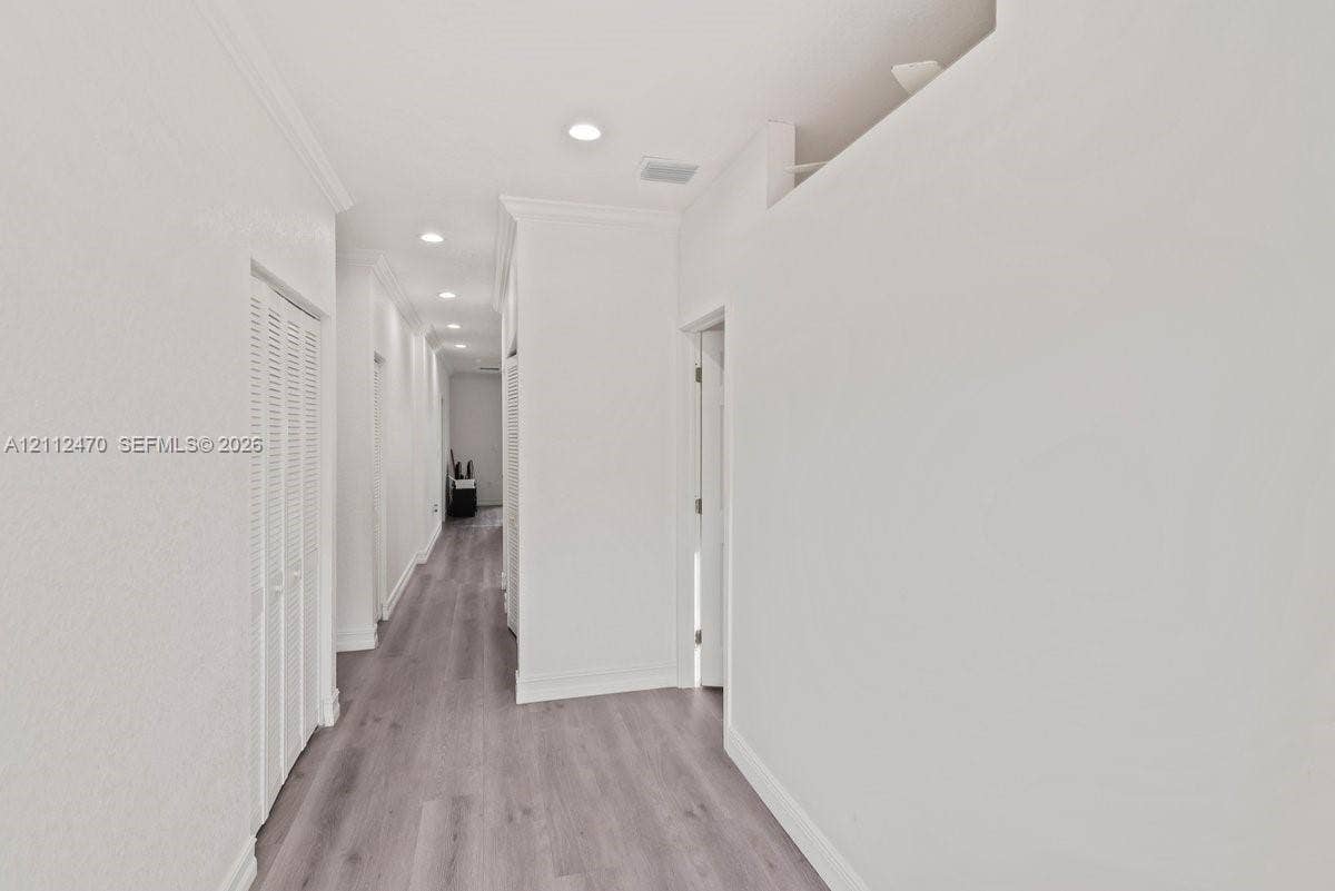Hallway featuring wood-finish flooring, recessed lighting, and louvered-door closets