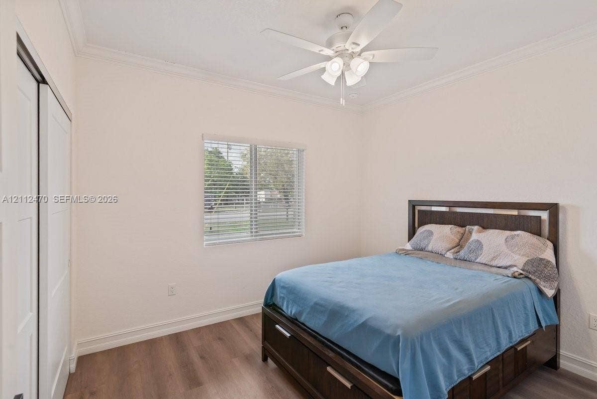 Bedroom featuring wood-finish flooring, crown molding, a white ceiling fan with integrated lighting, and closet with sliding panel doors