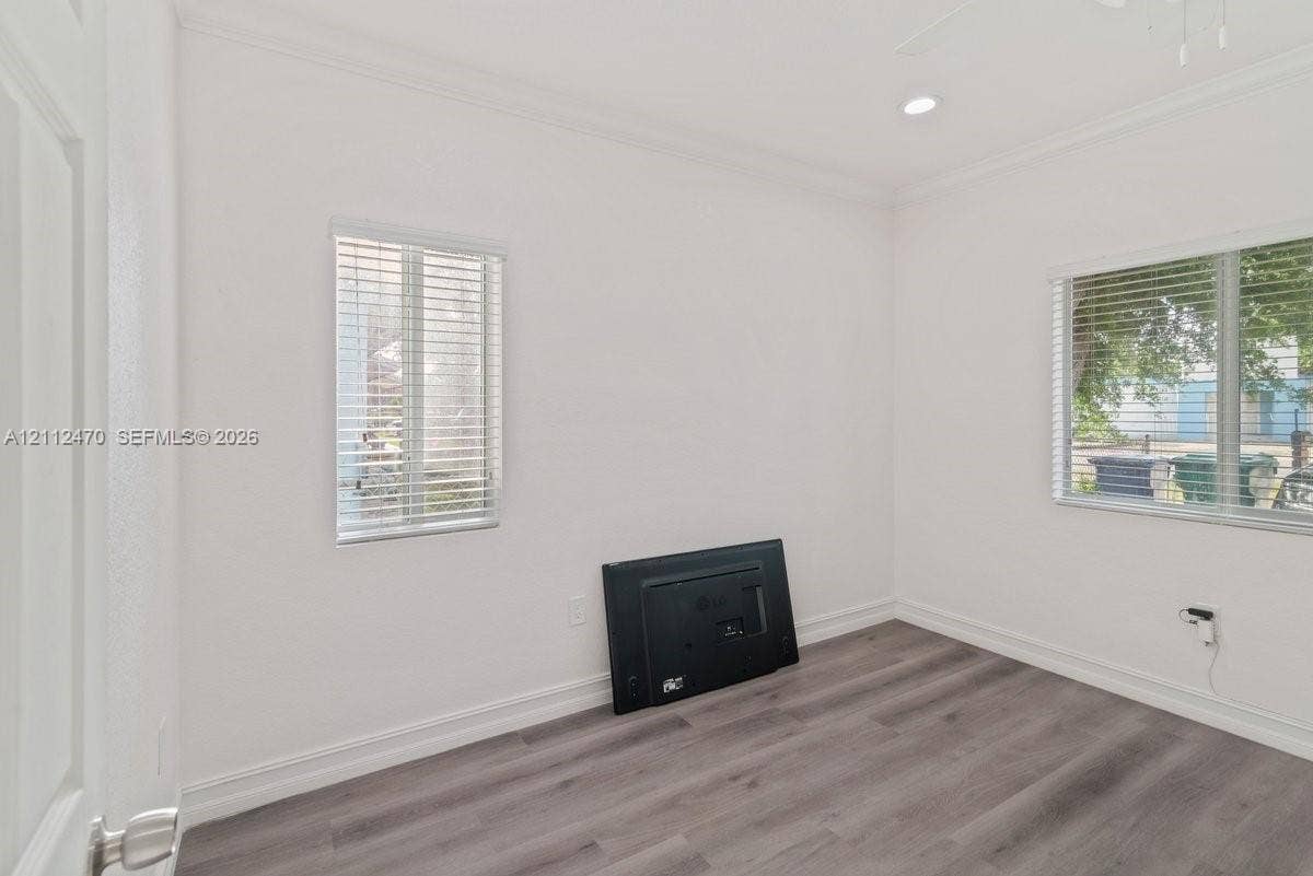 Neutral interior room featuring wood-finish flooring, crown molding, recessed lighting, and dual windows with horizontal blinds