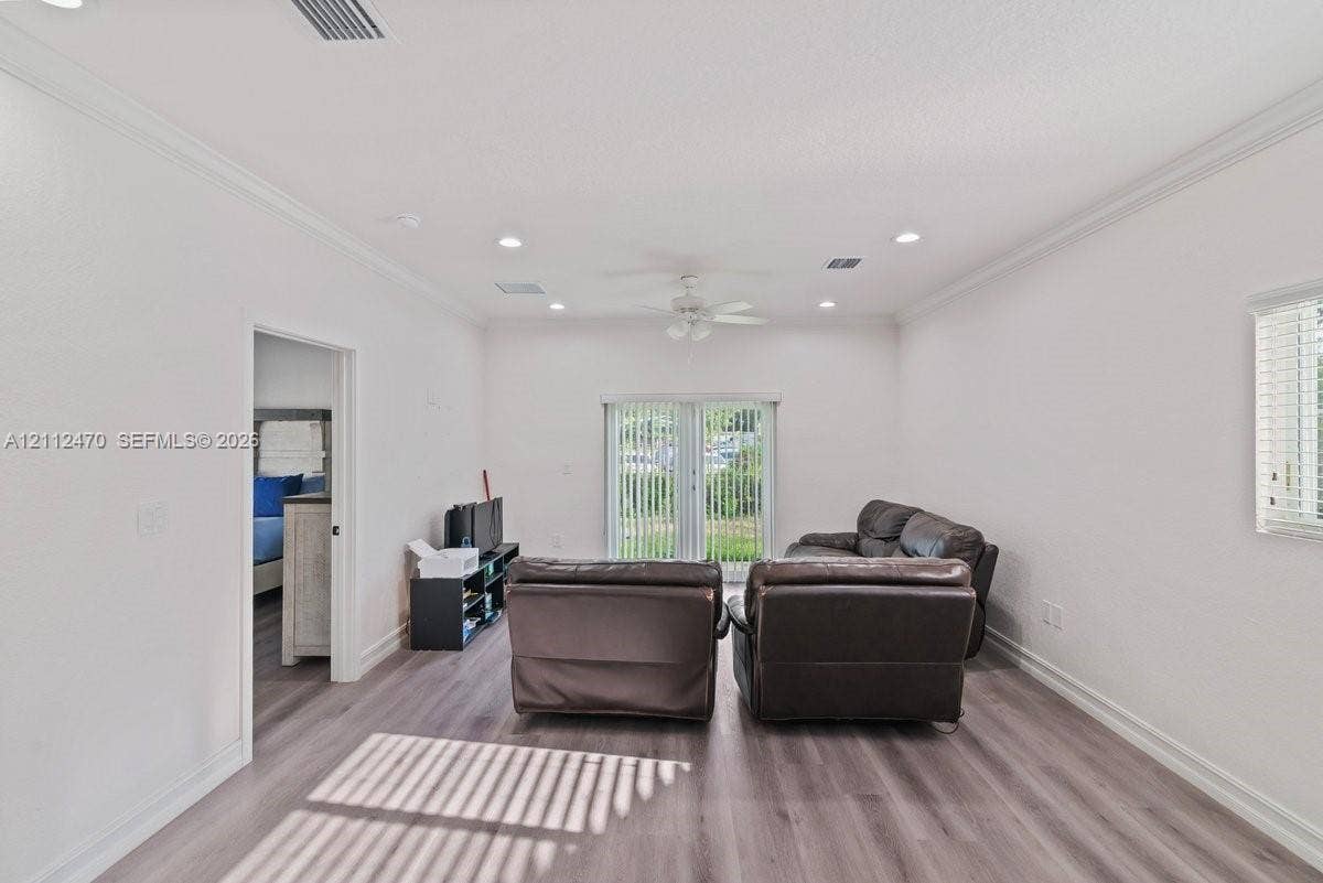 Living area featuring wood-finish flooring, recessed lighting, crown molding, a ceiling fan, and sliding glass doors with vertical blinds