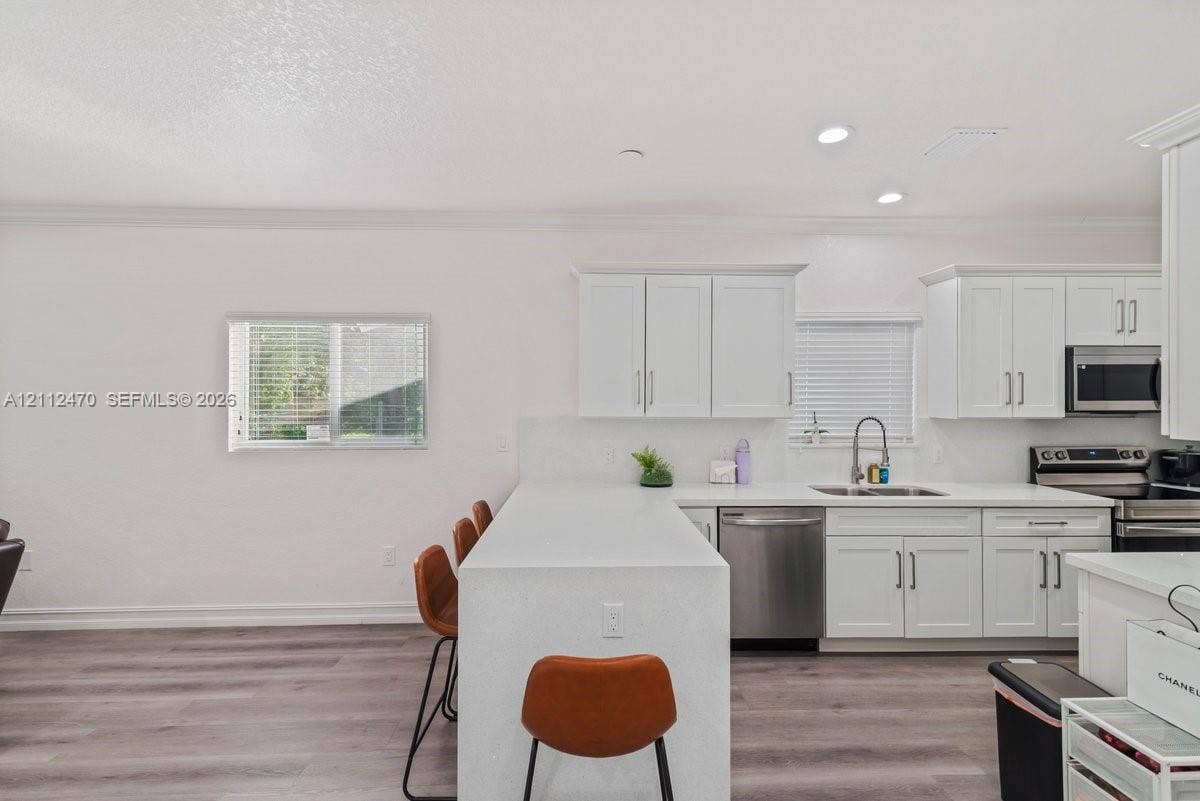 Kitchen featuring white cabinetry, solid-surface countertops, stainless steel appliances, and wood-finish flooring