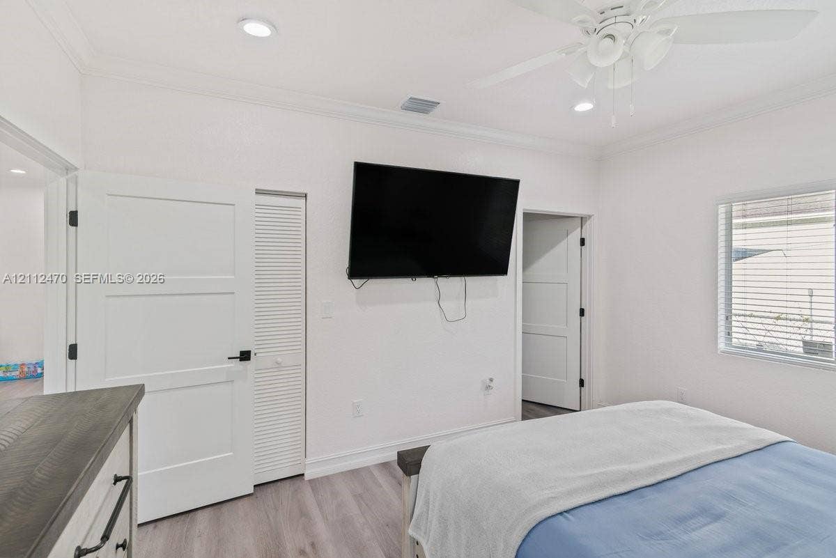 Room featuring recessed lighting, wood-finish flooring, crown molding, a ceiling fan, and louvered closet doors