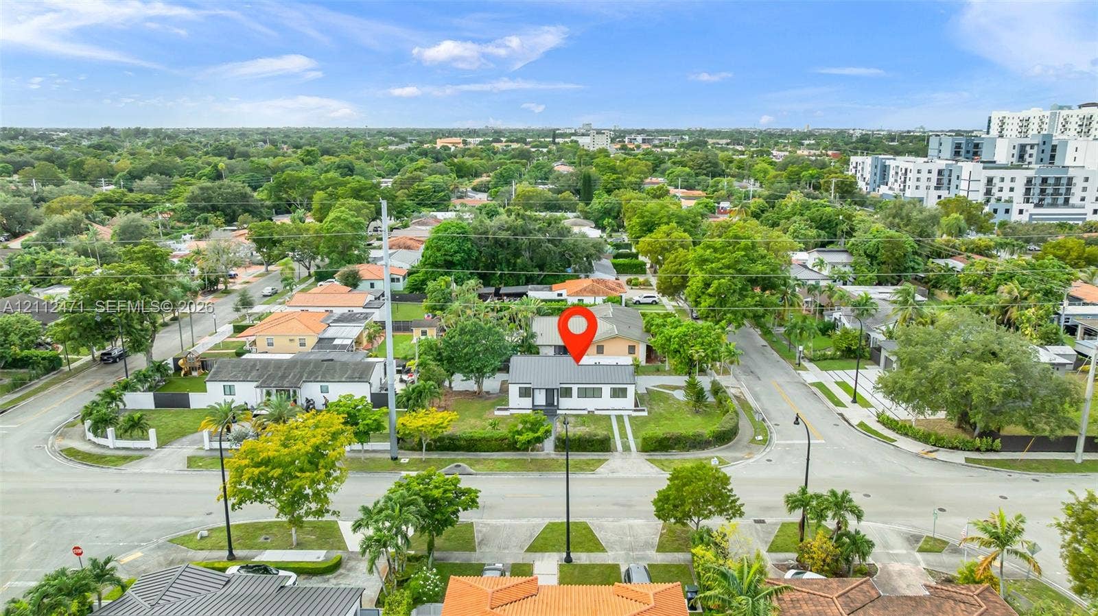 Aerial perspective of a detached single-story residence on a corner lot featuring a concrete driveway and mature perimeter landscaping