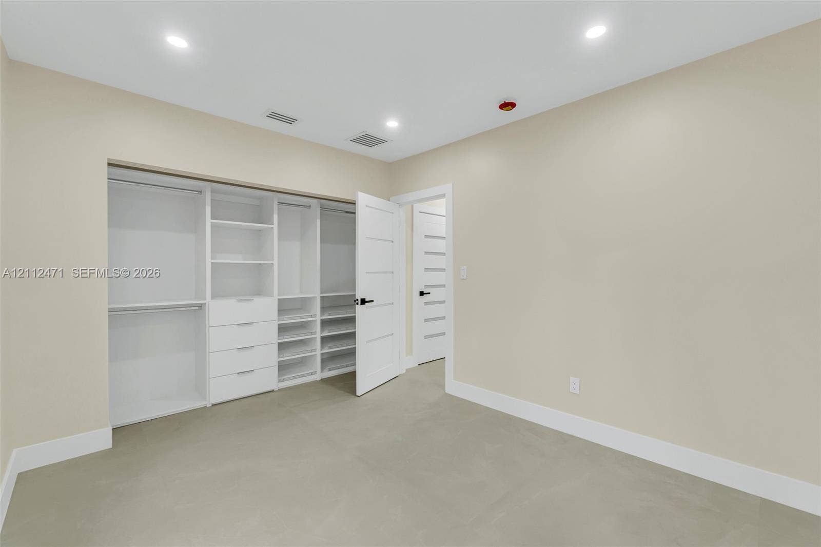 Customized walk-in closet featuring floor-to-ceiling white cabinetry, integrated drawer storage, and multiple shelving units, complemented by solid-core interior doors with matte black hardware and recessed lighting